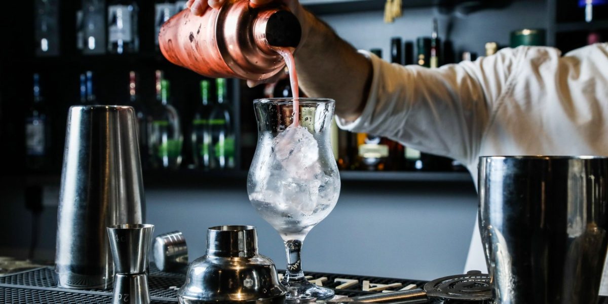 man-pouring-cocktail-from-shaker-in-the-glass-with-ice-bar-side-view.jpg